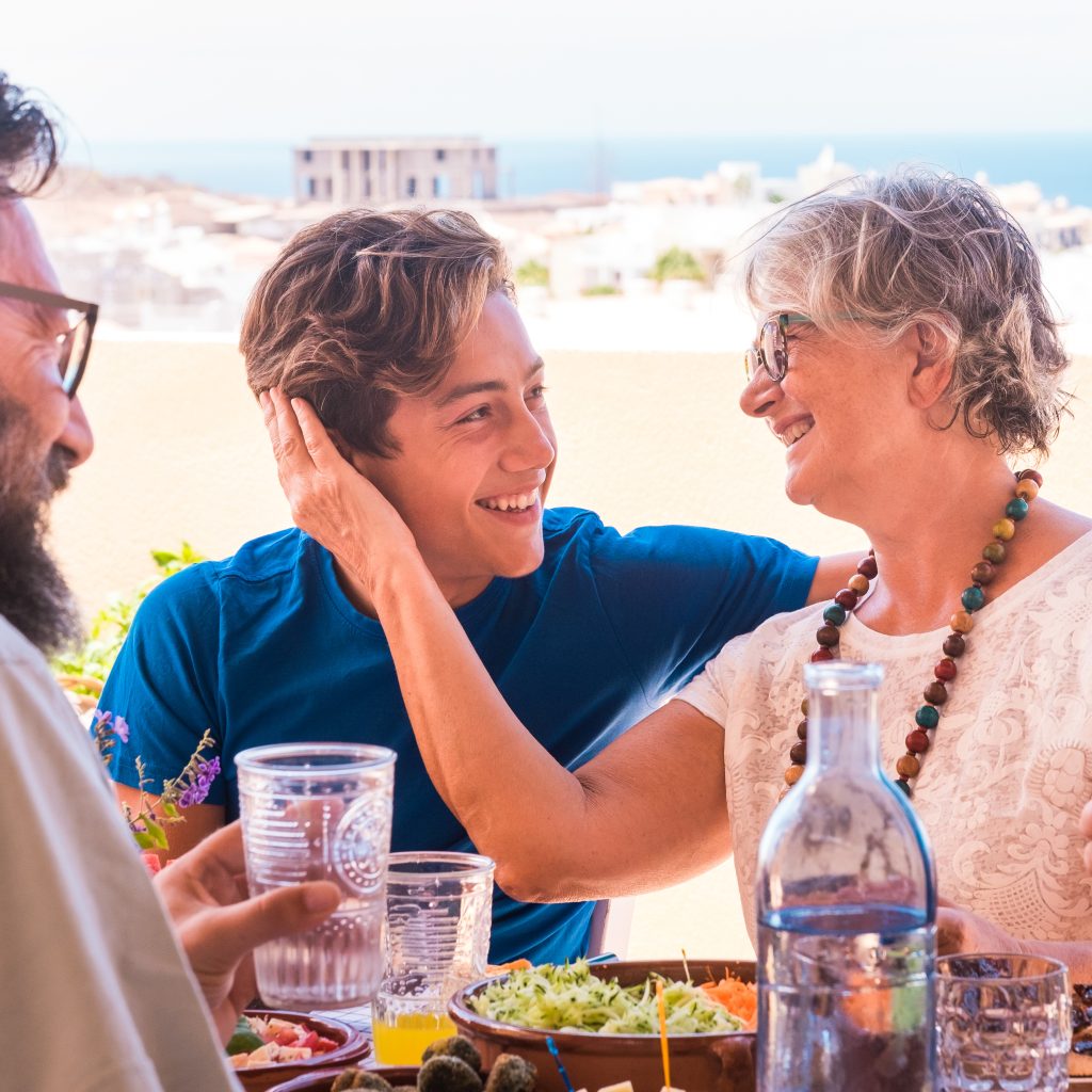 Group of multigenerational family, a tender gesture of affection between grandmother and grandson smiling and looking each other. Brunch together outdoor in the terrace
